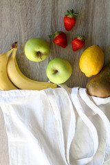 Canvas tote bag with bananas, apples, pear, lemon and strawberries. Top view.