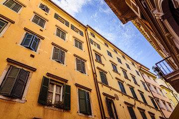 Fototapeta premium Bottom view of an old yellow building with green shutters on the windows with blue sky on the background
