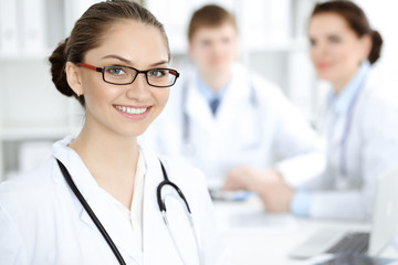 Happy smiling woman-doctor sitting and looking at camera at meeting with medical staff . Medicine concept