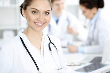 Happy smiling woman-doctor sitting and looking at camera at meeting with medical staff . Medicine concept