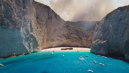 Photo sur Plexiglas Plage de Navagio, Zakynthos, Grèce Zakynthos Navagio Shipwreck Bay in Greece, One Of the Most Unique Beaches on Earth, Wildfires Burning in the Background