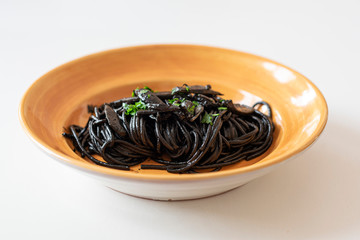 Italian pasta with black sauce of cuttlefish and parsley on yellow plate