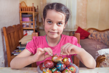 Fototapeta premium Portrait of a girl of 7 years old. A girl sits at a table, next to it is a plate with Easter eggs. Dark hair, brown eyes.