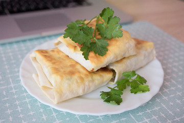 Pita with greens on a white plate on the wooden table near a computer, delicious breakfast made at home. Traditional Middle Easter fast food. Homemade dish. 