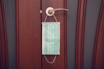 Protective medical mask hanging on the door handle. Quarantine concept.