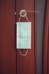 Protective medical mask hanging on the door handle. Quarantine concept.