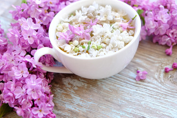 Cup of tea with lilac flowers on wooden background. Spring time. Vase with lilac. Copy space for text. The concept of holidays and good morning wishes.

