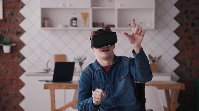 Adult man in wheelchair using vr helmet at home. male or teenager wearing VR goggles and playing video games in virtual reality. concept entertainment, celebral palsy, technology. 3d headset
