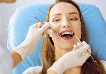 Smiling young woman with orthodontic brackets examined by dentist at dental clinic