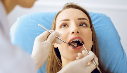 Smiling young woman with orthodontic brackets examined by dentist at dental clinic