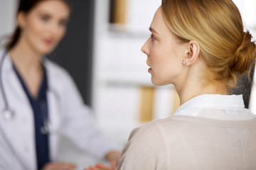 Fototapeta premium Friendly smiling female doctor and patient woman discussing current health examination while sitting in clinic. Medicine and healthcare concept