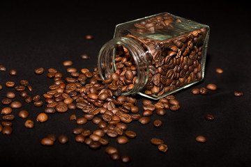 a glass jar of coffee beans lies on its side against a black background