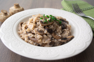 Classic Italian vegan mushroom risotto made with arborio rice, mushrooms, onion and garlic garnished with basil ribbons on a rustic wooden surface with a green napkin and a fork