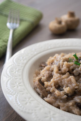 Classic Italian vegan mushroom risotto made with arborio rice, mushrooms, onion and garlic garnished with basil ribbons on a rustic wooden surface with a green napkin and a fork