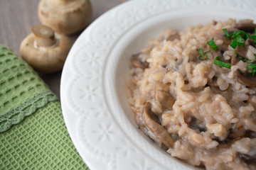 Classic Italian vegan mushroom risotto made with arborio rice, mushrooms, onion and garlic garnished with basil ribbons on a rustic wooden surface with a green napkin and a fork