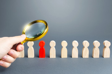 A hand with a magnifying glass studies a red person in a row of people. Identification, examination...