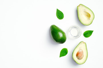Flat lay fresh avocado and bowl of essential oil with green leaves on white background. Top view natural avocado beauty product, skin care and body treatment concept
