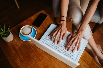  
Pretty young caucasian businesswoman drinking coffee and working on a laptop in a cafe