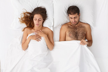 Family couple have problem of infertlity, man looks down under blanket, has erectile dysfunction...