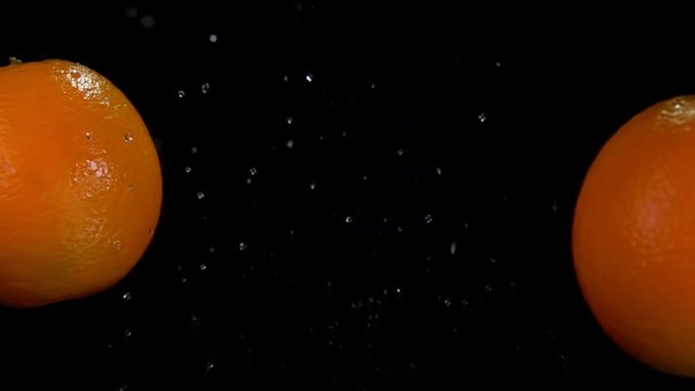 Two juicy oranges are flying and colliding with each other rising drops of water on the black background in slow motion