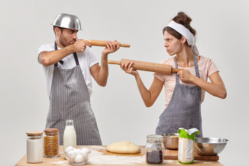 Horizontal shot of angry husband and wife feel like opponents, shoot at each other with rolling...