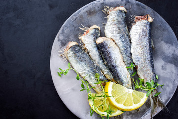 Fried sardines with lemon slices and herbs offered as top view on a modern design plate with copy space left