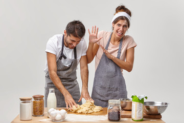 Funny woman and man make dough for pie, have cheerful faces, dressed in aprons, get culinary experience, have some problems, add ingredient not according to recipe. Cooking time, baking concept