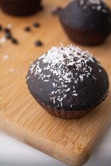 Chocolate glazed chocolate cocoa crazy cake muffins with coconut flakes on a wooden board with coconut flakes and chocolate chips sprinkled on it