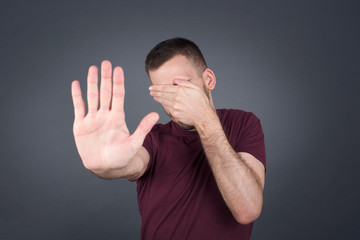 People, body language. Young European man covers eyes with palm and doing stop gesture, tries to hide from everybody. Don't look at me, I don't want to see, feels ashamed or scared.