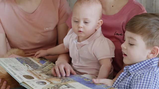 A lesbian family with two children and mothers isolated at home. Home education. They read a book with pictures.