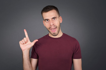 Close up portrait of pleasant looking blue eyed young man model has clever expression, raises one finger, remembers himself not to forget tell important thing.