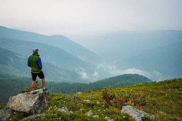 A man stands on a hill in front of a foggy mountain valley. Foggy weather high in the mountains in...
