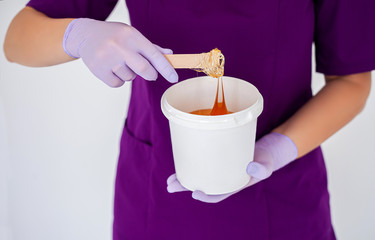 Women beautician holds jar wax of paste for sugar depilation shugaring, white background.