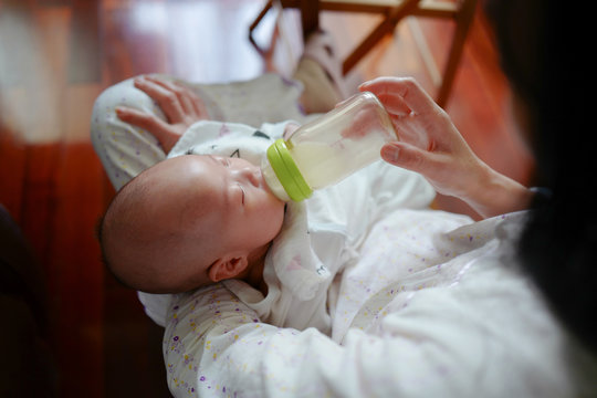 The baby drinks the breast milk in the bottle in the mother's arms.