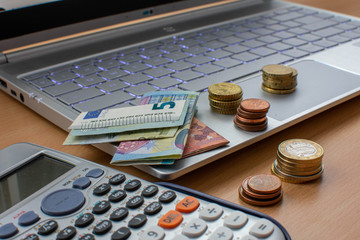 Grupos de monedas y billetes encima de un ordenador al lado de una calculadora  