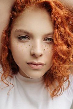 The portrait of the curly red hair girl with heart shaped fake freckles with her hands around the head