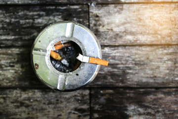 Metal ashtray with cigarette on wood table