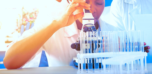 Young African female scientist, medic or tech tests patient samples with microscope in test lab....