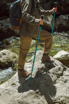 Woman with hiking poles. Trekking shoes on rocks and in runnig water.