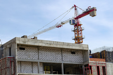 Fototapeta na wymiar Red tower crane on the construction of a brick house.
