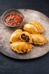 Traditionelle südamerikanische Empanada de Carne angeboten mit Chili Dip als closeup auf einem rustikalen Modern Design Teller