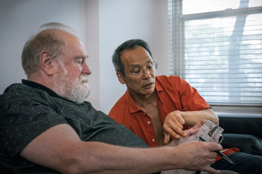 Senior Gay Man Helping Husband Solve Crossword Puzzle as Mental Exercise