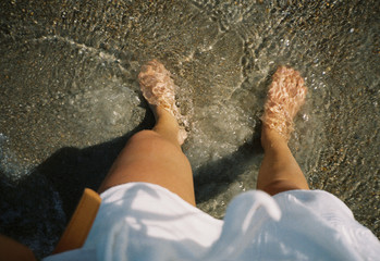 Standing barefoot at the shore covered by the ocean water