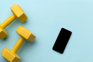 Flat lay top view yellow dumbbells and smartphone on blue background