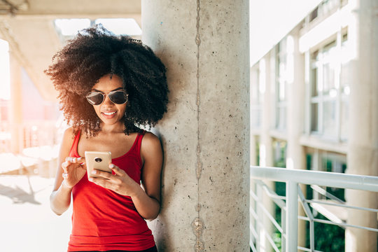 Young afro woman texting using a cellphone in urban scenery
