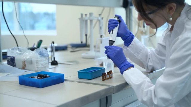 Female scientist is examining vaccine for coronavirus at table in pharmaceutical laboratory spbas. Woman chemist is testing new drugs using reagents, sitting at desk during working day in modern