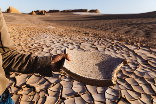 Male hand holding a piece of dry clay in the desert