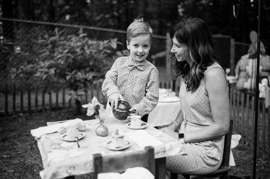 Formally dressed cute young boy serving his mother tea
