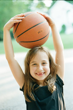 Portrait of a young happy girl holding a basketball on top of her head