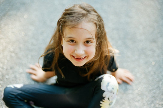 Portrait of a young happy girl sitting on patch of asphalt